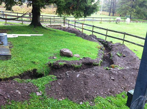 A shallow trench hooking out through the yard and leading to the outdoor wood boiler site. 