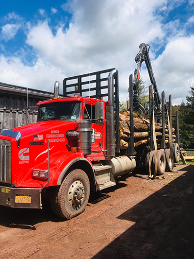 A red log truck with a load of log-length firewood in the driveway.