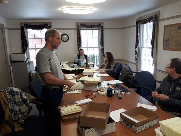 Five members of the WAC Forestry Program at a long boardroom table stuffing envelopes with CAI surveys and cover letters. Look out for paper cuts!