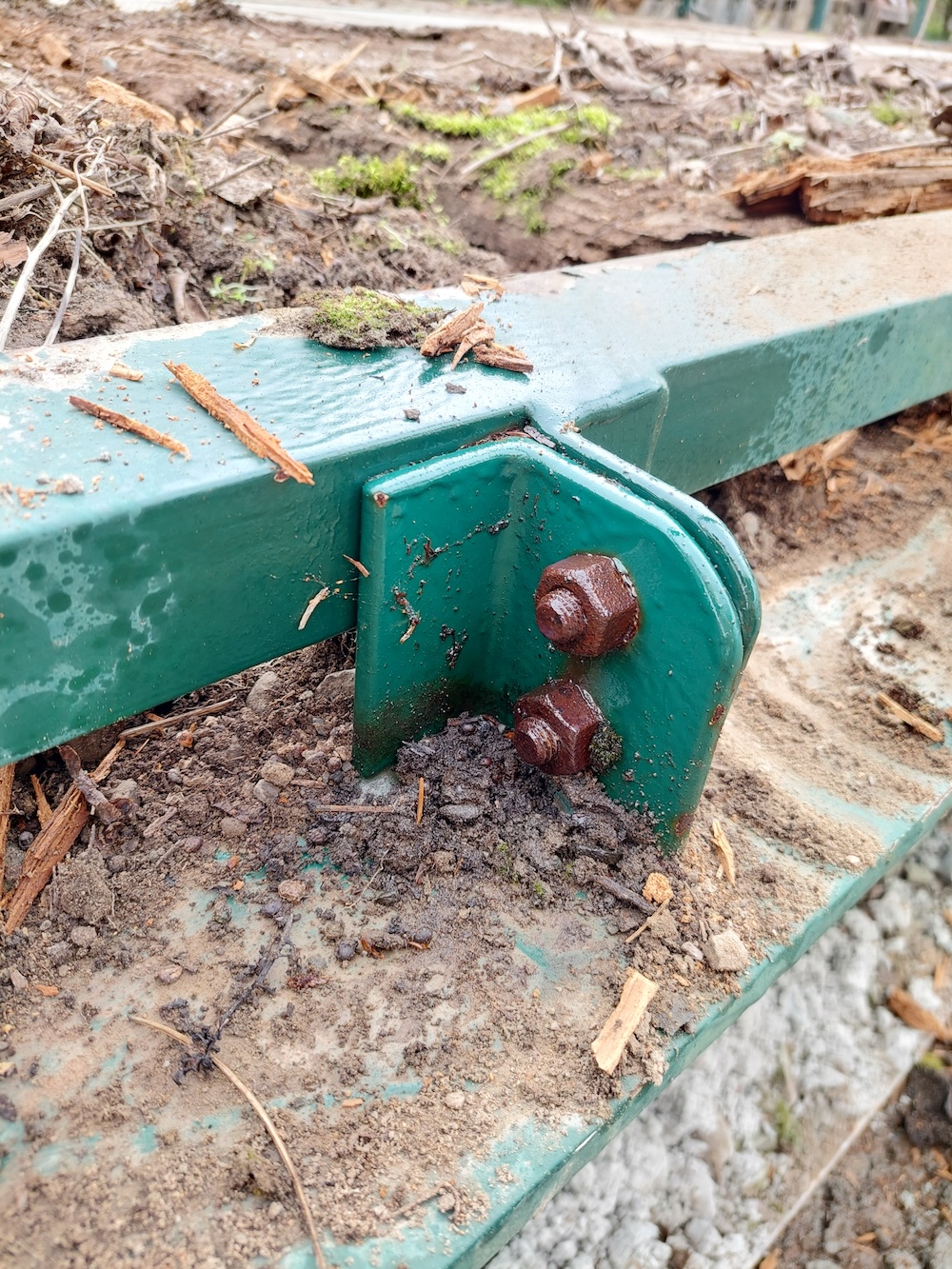 A close-up of the nuts and bolts that hold the bridge frame tight against the wooden decking, which sits inside the frame. Spray lubricant has been applied to the rusty hardware.