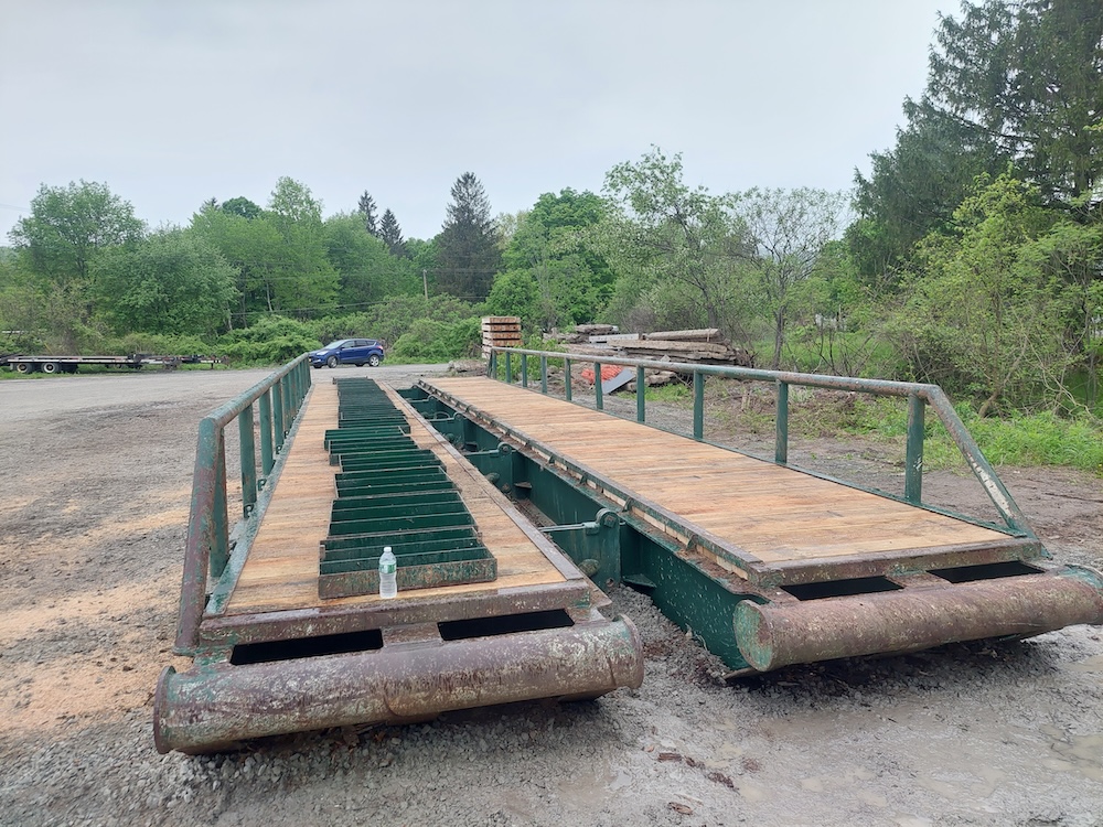 A 50-foot-long, hinged portable bridge with new red oak decking. The center panels have been removed and placed on one side of the bridge.