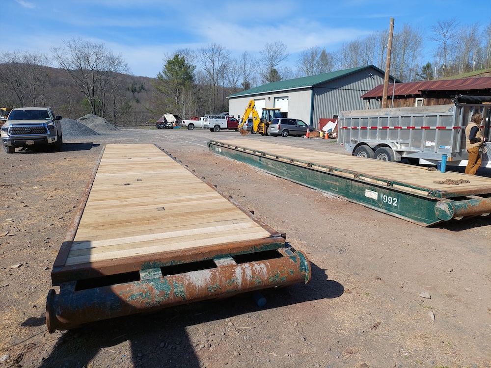 New decking, 40-foot bridge. Two 40-foot, steel-framed bridge panels lay in a construction yard with new, light-colored white oak decking.